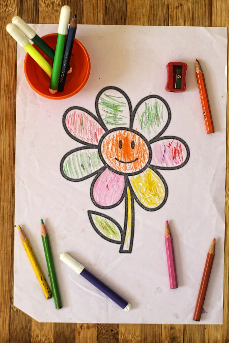 A flower coloring page colored in by a young child, with pencils and markers