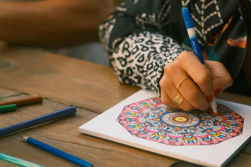 Hands coloring a detailed mandala with a blue marker