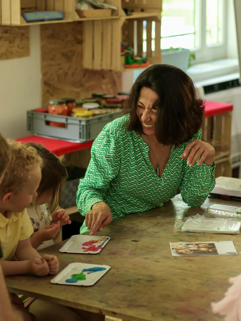 A preschool teacher laughing with two young children at a craft table